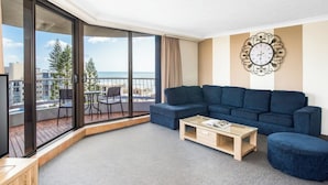 A modern living room with a large sofa, a coffee table, and a view of the city through floor-to-ceiling windows.