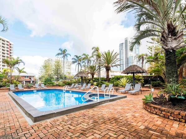 A swimming pool with lounge chairs, surrounded by palm trees and a brick patio. - Breakfree Acapulco Surfers Paradise (Gold Coast)