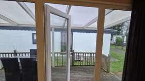 Ein überdachter Außenbereich mit einer Schiebetür, einem Holzdeck und Blick auf eine Wohngegend.