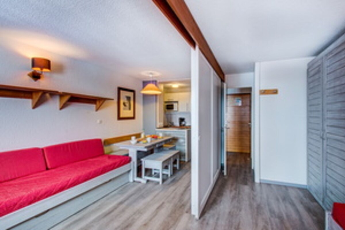 Una habitación con un sofá rojo, una mesa de comedor y una zona de cocina.