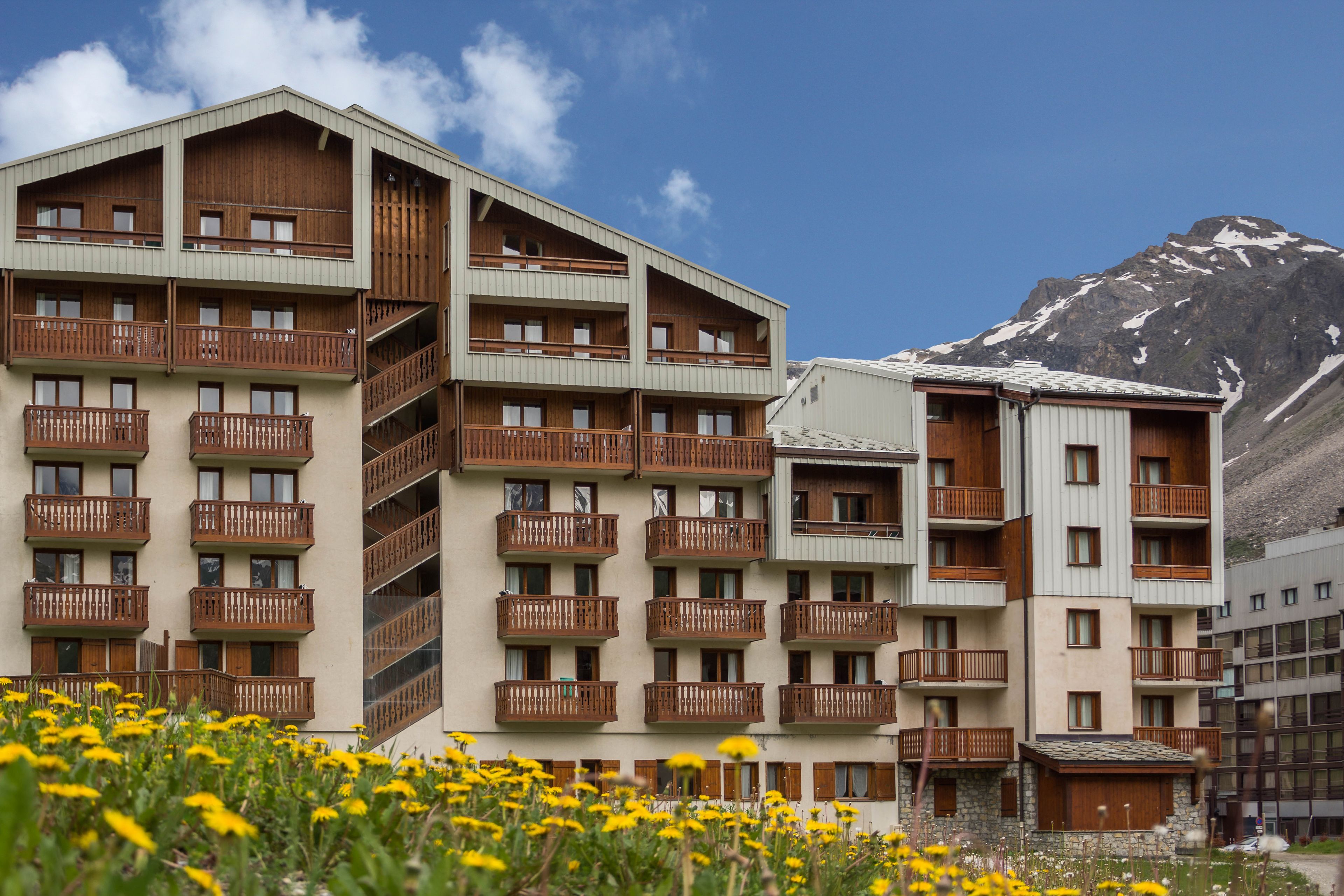 Ein mehrstöckiges Hotel mit Balkonen, einem Berg im Hintergrund und einem Blumenbeet im Vordergrund.