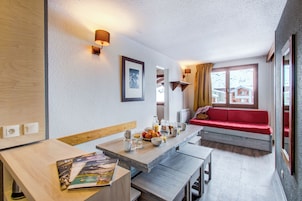 Una sala moderna con una mesa de comedor de madera, un sofá rojo y un ventanal con vistas a casas.