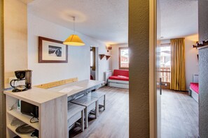 A modern kitchen with a coffee maker, a dining table with benches, a hanging light fixture, and a red sofa in the background. - Résidence Le Borsat IV - Vacanceole (Tignes)