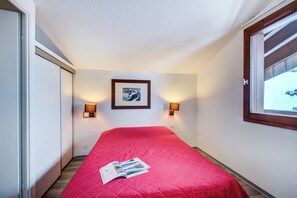 Habitación de hotel con una colcha roja, un cuadro en la pared y dos lámparas fijadas a la pared.