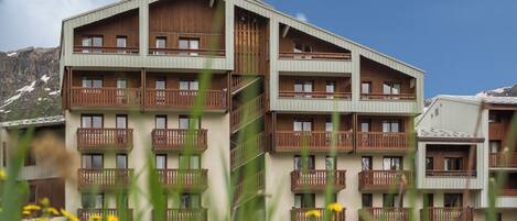 Un hotel a più piani con balconi, facciata in legno e montagne sullo sfondo.
