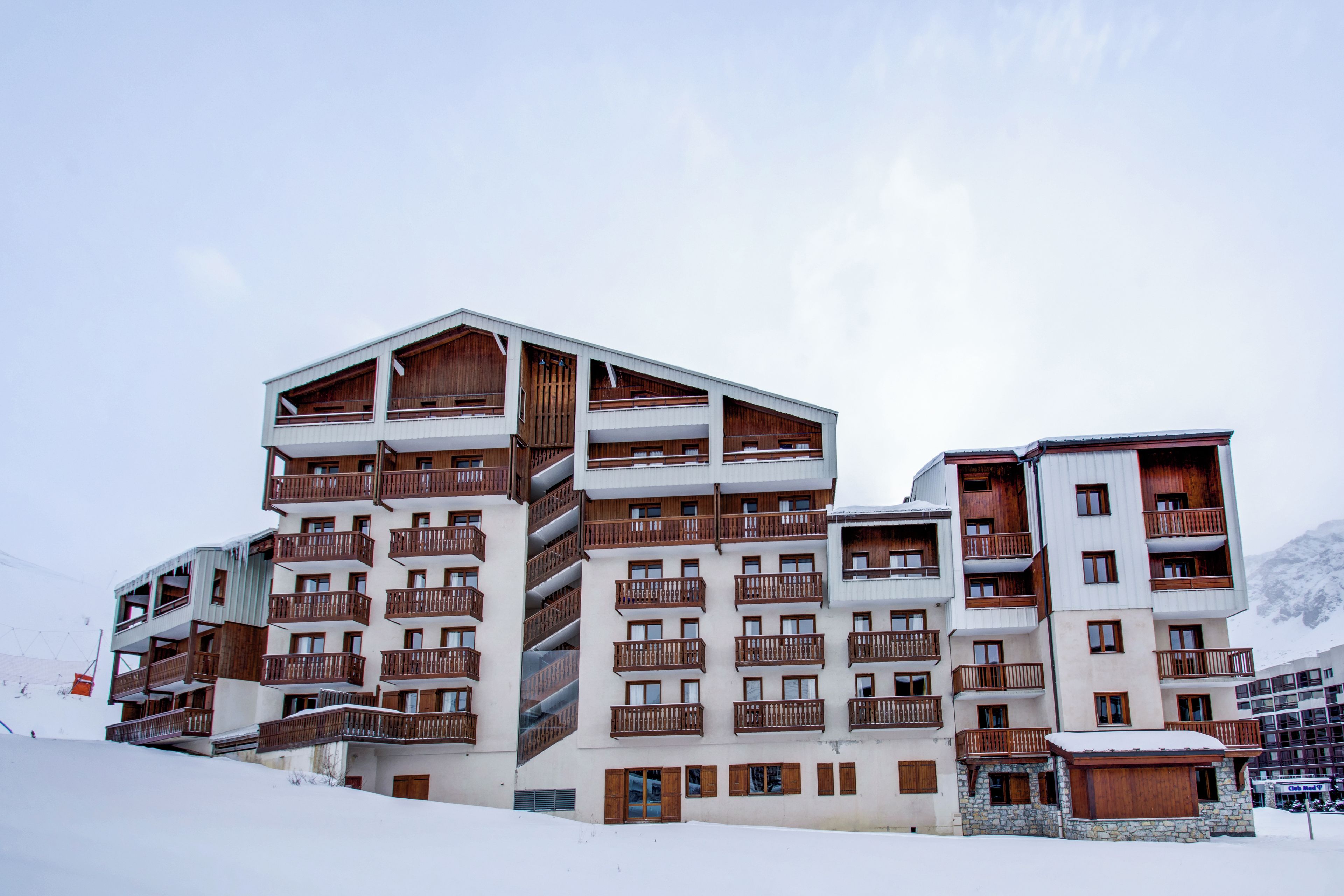 Un hôtel à plusieurs étages doté de balcons, avec un télésiège visible en arrière-plan et un paysage enneigé.