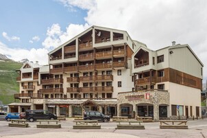 Un hotel de varios pisos con balcones, mobiliario exterior y fachada de piedra.