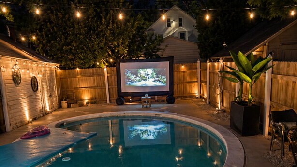 A backyard with a swimming pool, a projector screen, and string lights.