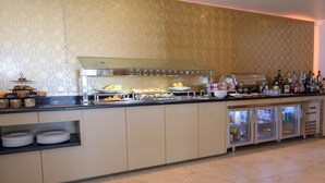 A buffet bar with various food items, a refrigerator with beverages, and a decorative wall.
