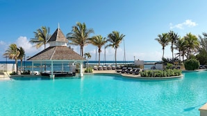 A pool with lounge chairs, palm trees, and a gazebo overlooking the ocean.