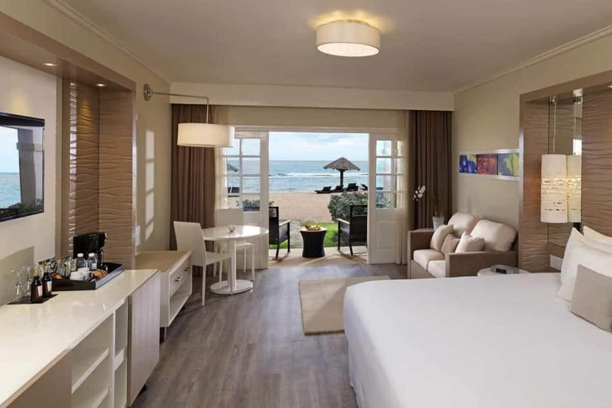 Quarto de hotel com cama, escrivaninha, cadeira, mesa pequena e vista para a praia.
