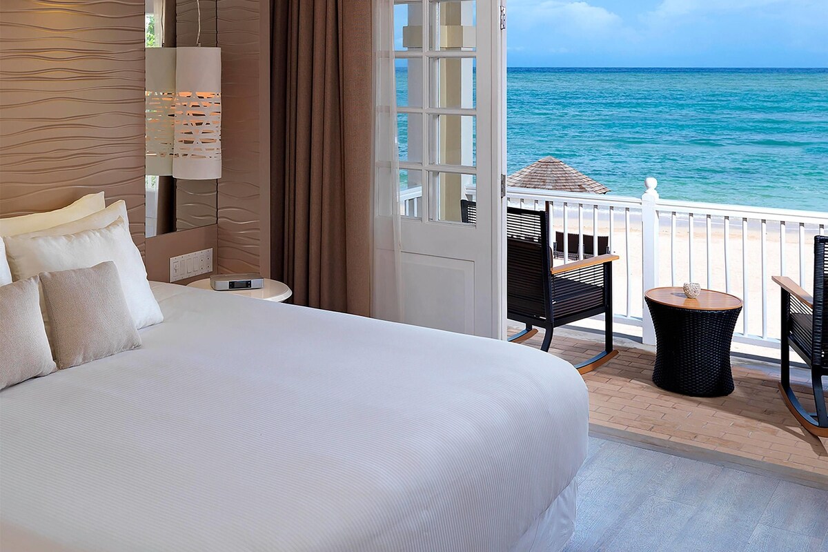 Une chambre d’hôtel dotée d’un grand lit, offrant une vue sur l’océan, d’un balcon avec mobilier d’extérieur et d’un design moderne.