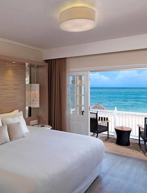 Une chambre d’hôtel dotée d’un grand lit, offrant une vue sur l’océan, d’un balcon avec mobilier d’extérieur et d’un design moderne.