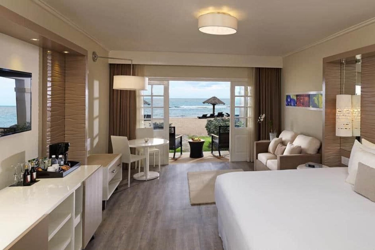 Une chambre d’hôtel avec un lit, un bureau, une chaise, une petite table et une vue sur la plage.