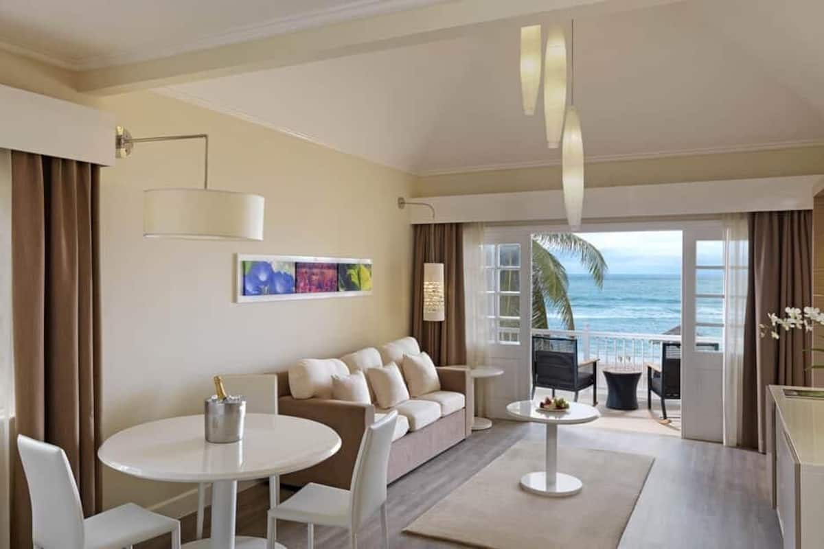 Quarto de hotel moderno com varanda, um sofá, uma mesa de jantar e uma televisão.