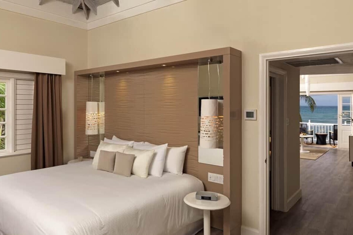 Une chambre d’hôtel avec un grand lit, une petite table de chevet, un miroir et une vue sur l’océan.