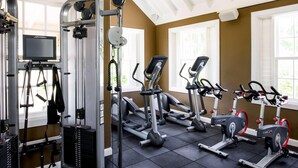 A gym with exercise equipment, a TV screen, and windows with blinds.