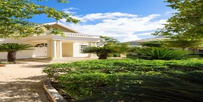 A building with a white facade, columns, and a garden with various plants. - Melia Braco Village (Rio Bueno)