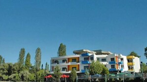 Un immeuble à plusieurs étages, doté de balcons et d’un toit plat, se dressant sous un ciel d’un bleu limpide.