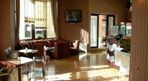 Un vestíbulo de hotel con una zona de estar, un televisor montado en la pared y un mostrador con una computadora.