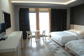 Habitación de hotel con escritorio, dos camas, televisor y ventana con cortinas.