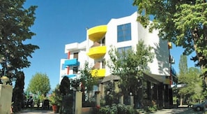 Un edificio de varios pisos con balcones, rodeado de árboles y un cielo despejado.