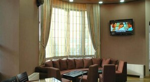 Una sala de estar con un sofá de cuero marrón, un televisor de pantalla plana montado en la pared y un ventanal con cortinas.