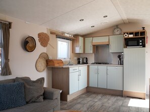 Eine kleine Küche mit Einbauherd, Mikrowelle und Spüle. Es gibt einen Holzschrank und ein kleines Regal mit einer Uhr und einem Telefon.