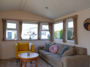 Ein Zimmer mit einer Couch, einem gelben Sessel, einem runden Holztisch und drei mit Vorhängen versehenen Fenstern.