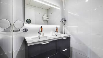 A modern bathroom with a large mirror, two sinks, a hairdryer, and a towel rack.
