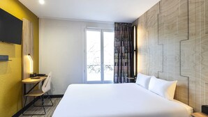 Habitación de hotel con una cama grande, un escritorio con silla, un televisor montado en la pared y una ventana con cortinas.