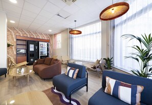 A modern lobby with seating areas, a vending machine, and large windows. - B&B Hotel Perpignan Centre 3 Étoiles (Perpignan)