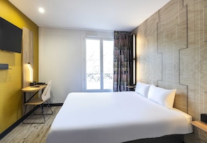 A hotel room with a large bed, a desk with a chair, a television mounted on the wall, and a window with curtains. - B&B Hotel Perpignan Centre 3 Étoiles (Perpignan)