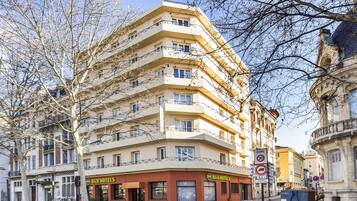 Un hotel de varios pisos con balcones, una señal de 'Zona 30' y un letrero que indica '3 habitaciones'.
