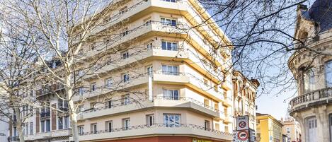 Un hotel de varios pisos con balcones, una señal de 'Zona 30' y un letrero que indica '3 habitaciones'.