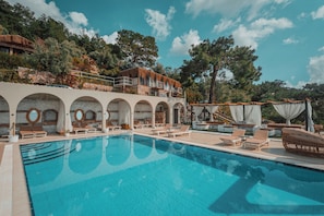 Una piscina con sillones de descanso, un muro de piedra y un edificio con balcones.