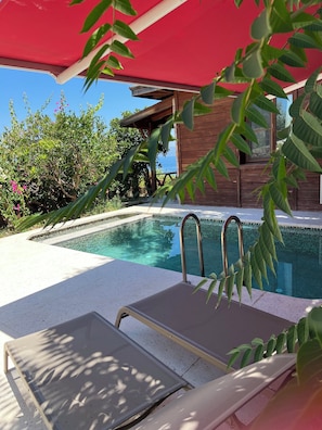 A poolside area with a lounge chair, a red umbrella, and a wooden building in the background. - Zakros Hotel Lykia (Fethiye)