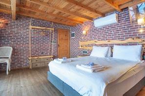 Habitación con pared de ladrillo, vigas de madera en el techo, cama con ropa blanca, cabecero de madera y un columpio colgante.