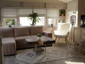 Uma sala de estar com sofá, mesa de centro, poltrona, televisão e uma planta.