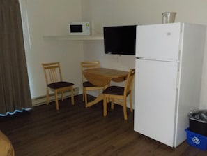 A small kitchen with a microwave, a refrigerator, a wooden table, and two chairs.