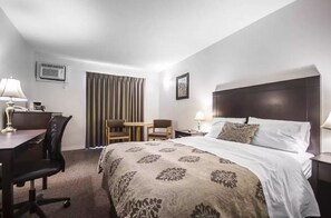 A hotel room with a bed, a desk, two chairs, a small table, and a nightstand with a lamp. - Econo Lodge Vernon Area (Vernon)