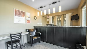 A hotel lobby with a reception desk, two chairs, a clock, and a television mounted on the wall. - Econo Lodge Vernon Area (Vernon)