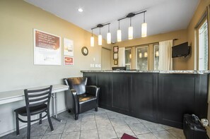 Eine Hotlellobby mit einer Rezeption, zwei Sesseln, einer Uhr und einem an der Wand befestigten Fernseher.