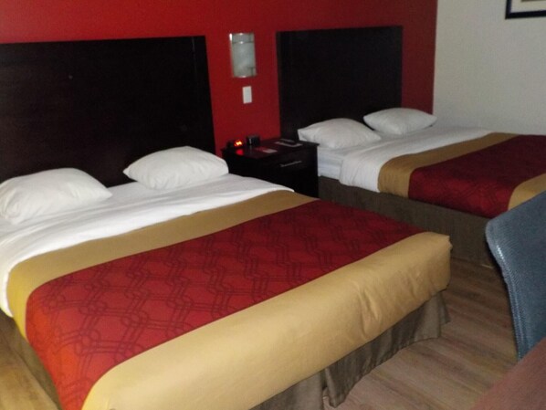 Ein Hotelzimmer mit zwei Betten, jeweils mit weißer Bettwäsche und roten sowie beige farbenen Überwürfen.