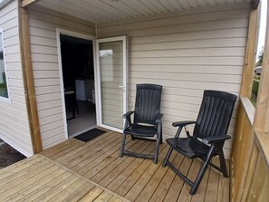 Eine überdachte Veranda mit zwei Stühlen, eine Glastür mit Schieberiegel, die zu einer Küche führt, und eine Holzterrasse.