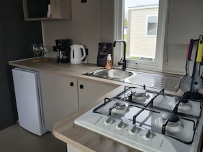 Eine kleine Küche mit Kühlschrank, Gaskochfeld, Spüle und Fenster.