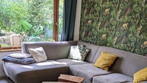 Uma sala de estar moderna com um sofá modular cinza, uma pequena mesa de centro de madeira, uma poltrona de vime e papel de parede estampado.
