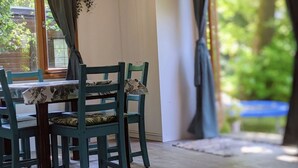 Espaço de refeições com mesa, cadeiras, luminária pendente e vista para o verde lá fora.