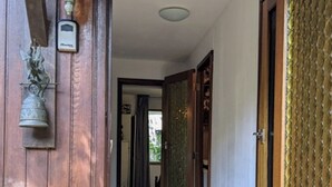 Um corredor de madeira com um tapete estampado, um sino de metal e uma porta com painel texturizado.