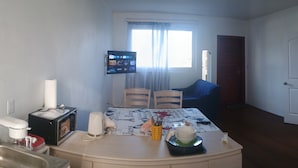 A small room with a kitchenette, a dining table with chairs, a TV, and a bed with a floral bedspread.